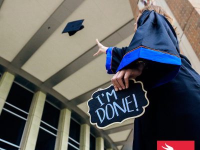 persona graduada de la universidad aventando la toga caqrgando un letrero de graduada